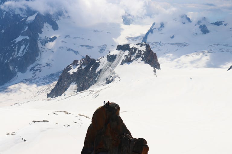 Two hikers atop a rock with Mont Blanc's snowy expanse in the background, capturing summer mountaineering spirit.